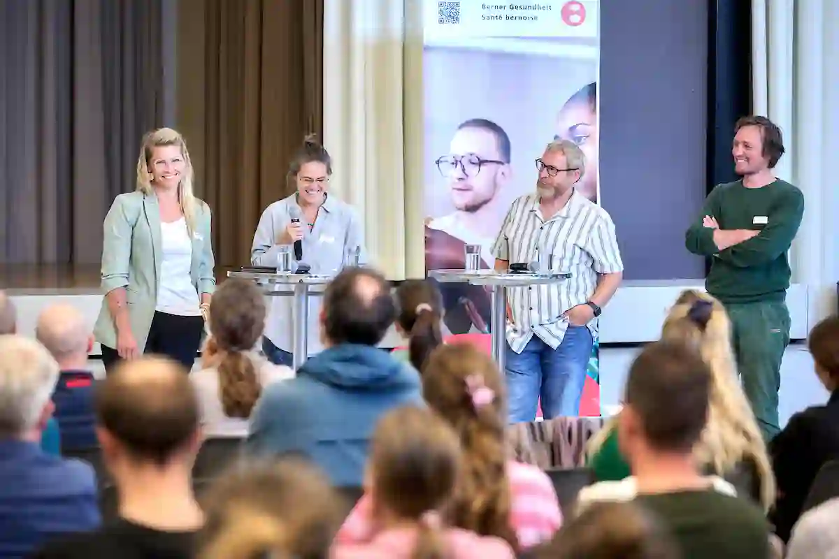 Vier Personen stehen nebeneinander auf einer Bühne. Das Publikum sitzt.