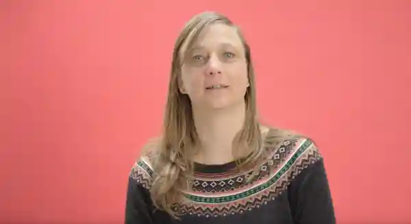 Portraitaufnahme einer weiblich gelesenen Person vor rotem Hintergrund.